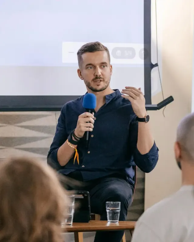 Olek Uznański speaking at a product event, holding a microphone
